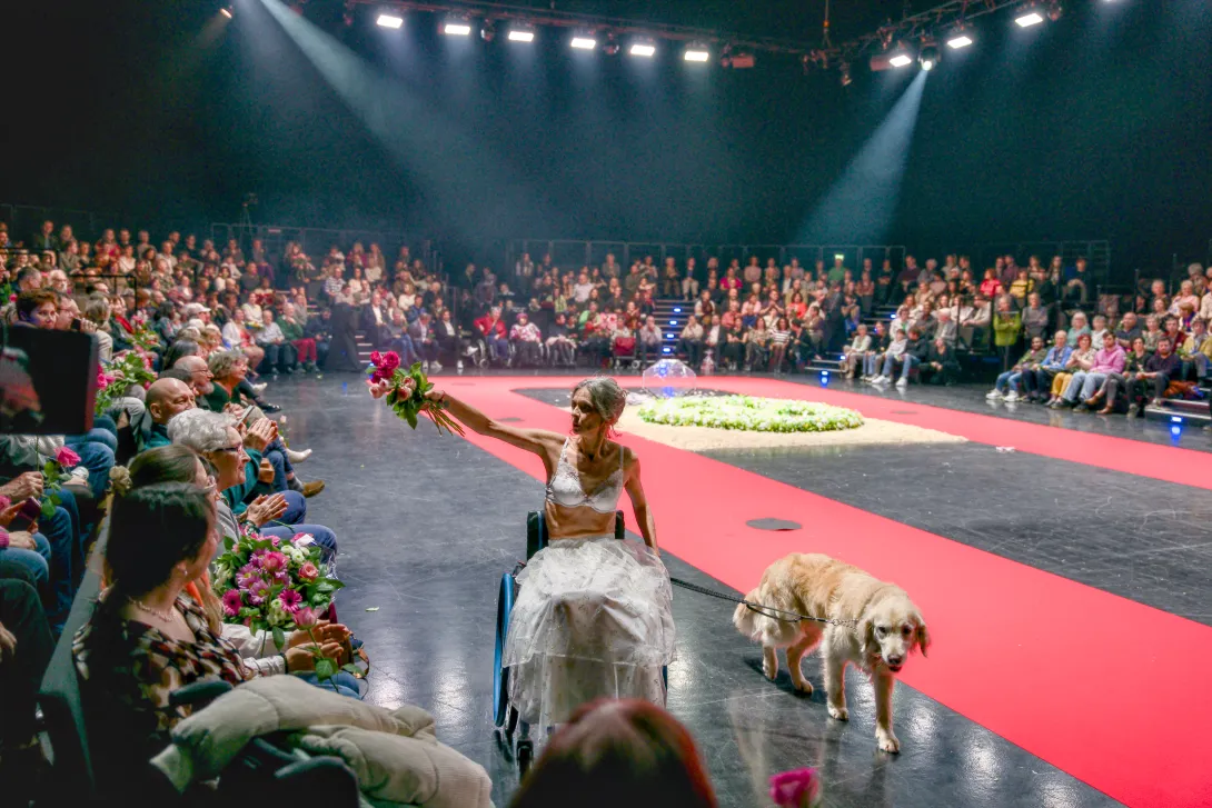 Une personne en situation de handicap défile avec son chien sous les applaudissements du public